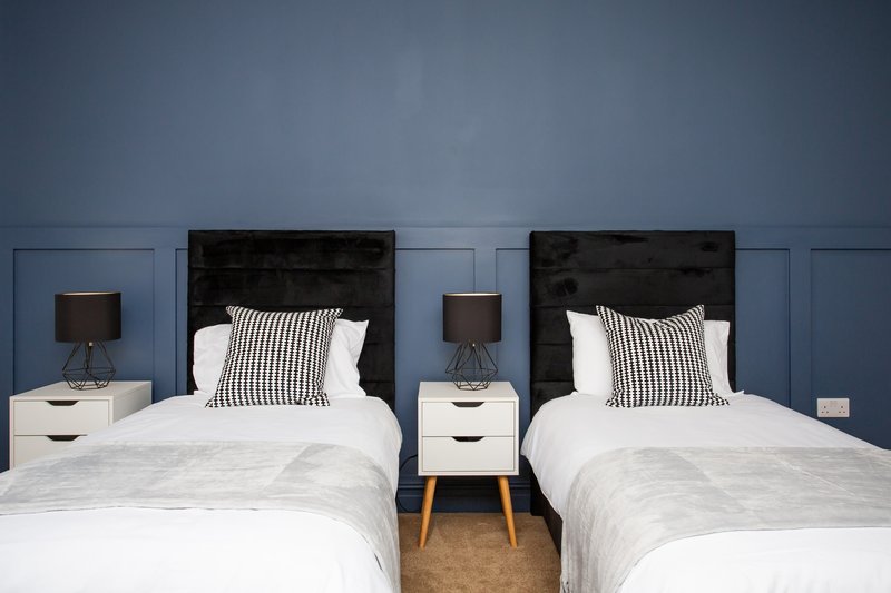 Twin bedroom with white bedding, striped pillows, black headboards and blue panelled walls