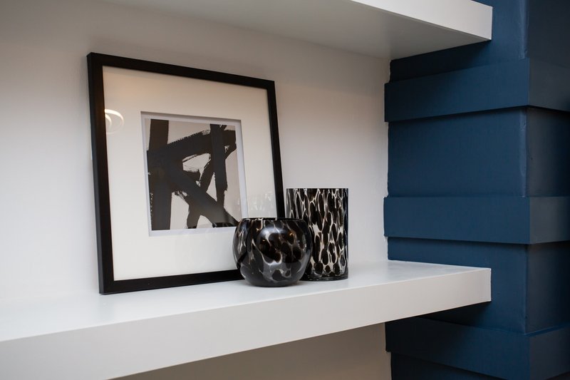 White floating shelf with framed abstract artwork, decorative vase and patterned object