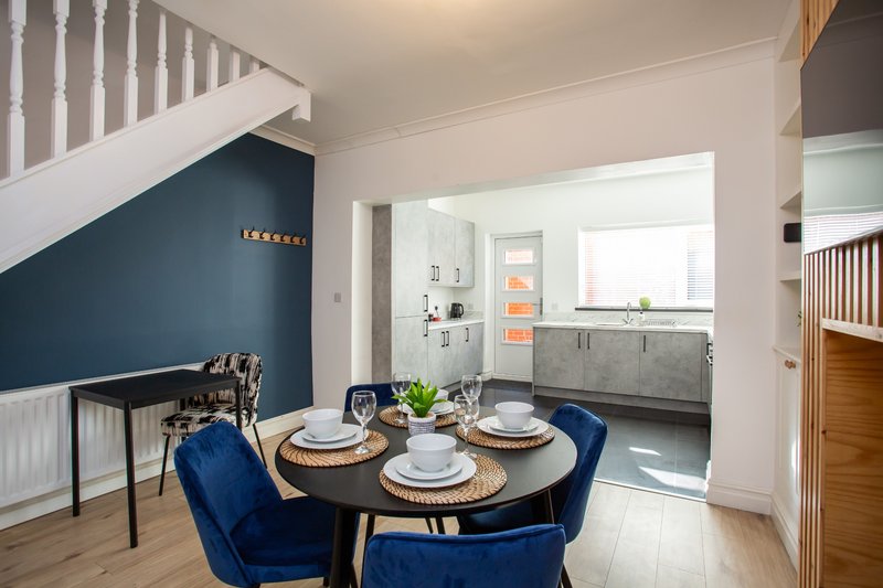 Modern dining area with round black table, blue velvet chairs, and open-plan kitchen visible through doorway