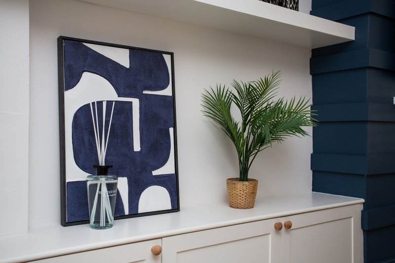 White shelf with abstract framed art, potted plant, and glass vase with dried flowers