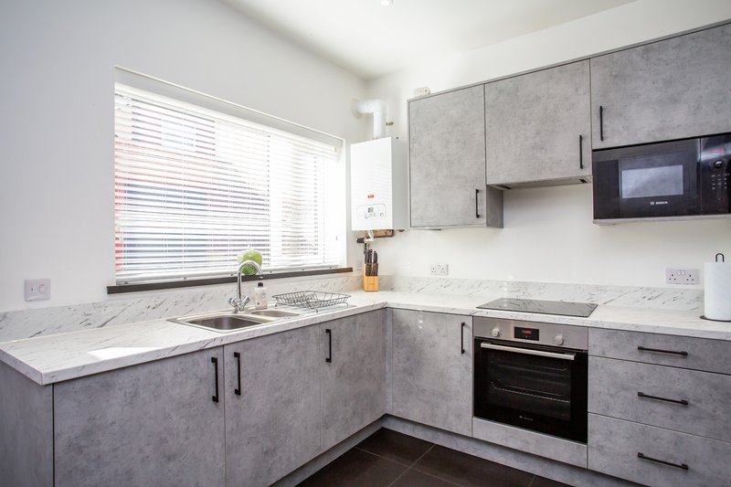 Modern kitchen with grey cabinetry, white countertops, integrated appliances and window with blinds