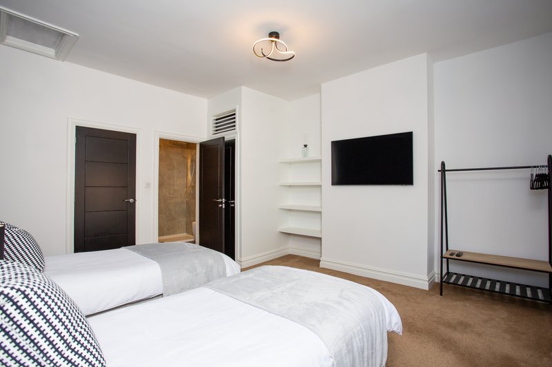Modern bedroom with two beds, wall-mounted TV, white shelving and dark doors