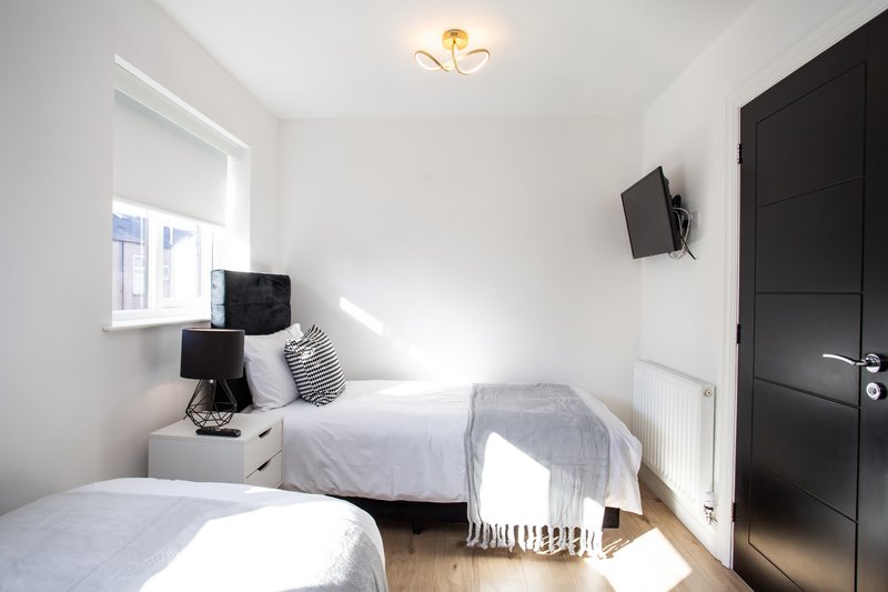 Bright bedroom with two single beds, white bedding, black bedside table and wall-mounted TV