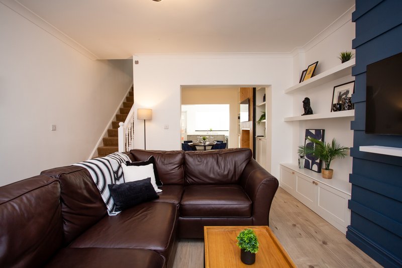 Modern living room with brown leather sectional, wooden coffee table, built-in shelving, and staircase