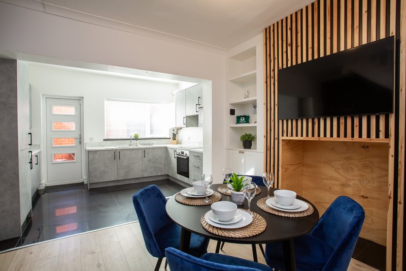 Modern dining area with round black table, blue chairs and open-plan kitchen with gray cabinetry