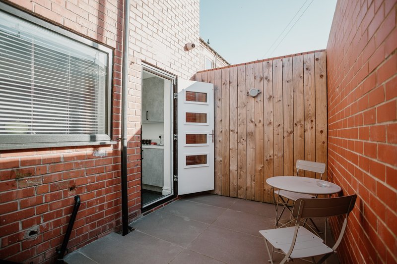 Brick courtyard with wooden fence, two chairs, and door to interior space