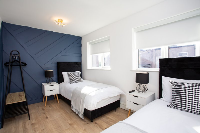 Bright modern bedroom with two single beds, blue accent wall, wooden floor and white furniture