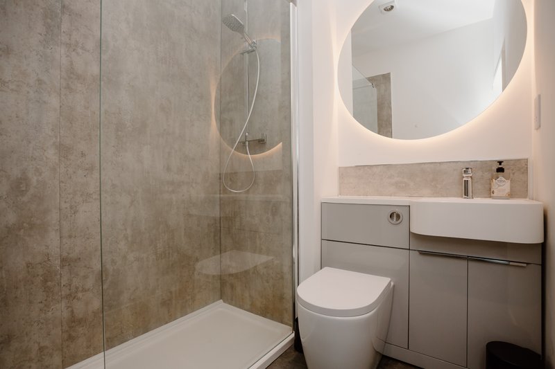 Modern bathroom with walk-in shower, illuminated mirror, white toilet and grey vanity unit