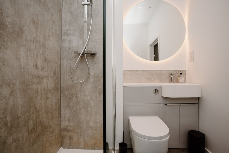Modern bathroom with walk-in shower, round illuminated mirror, white toilet and sink vanity