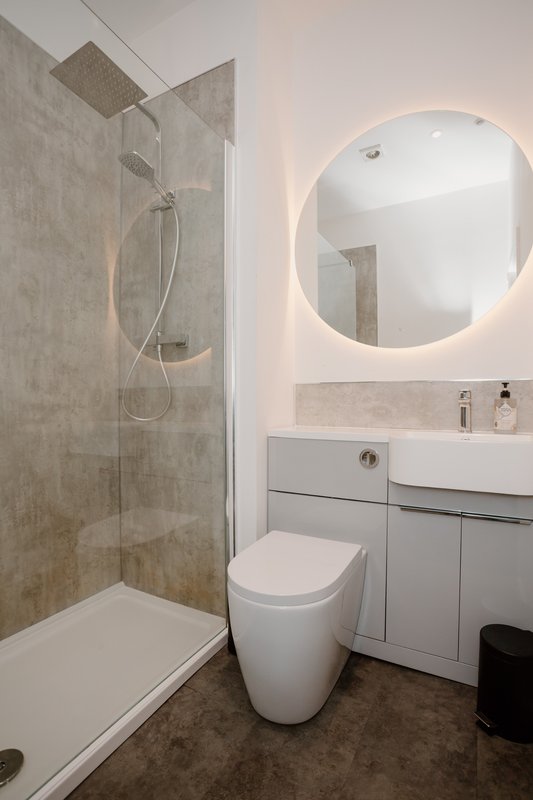 Modern bathroom with walk-in shower, toilet, illuminated round mirror and grey vanity unit