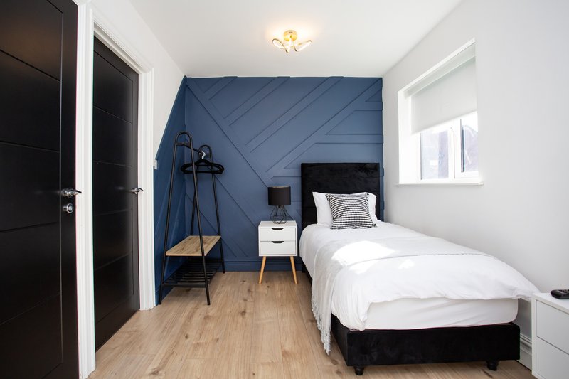 Modern bedroom with single bed, blue accent wall, wooden floor and pendant chair