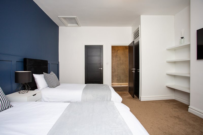 Modern bedroom with two single beds, blue accent wall, white shelving and dark doors