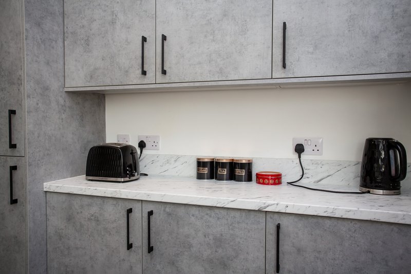 Modern kitchen countertop with kettle, toaster, jars and appliances against marble splashback