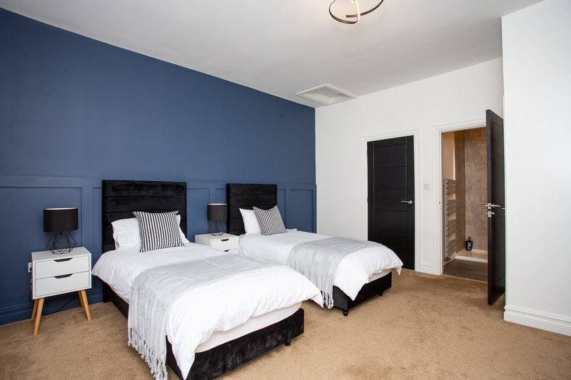 Bedroom with two single beds, blue accent wall, white bedding, wooden nightstand and modern ceiling light