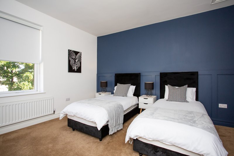 Bright twin bedroom with two single beds, blue accent wall, and large window