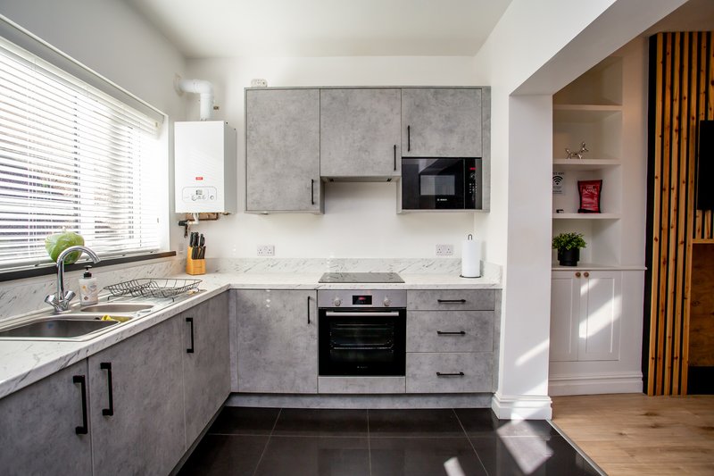 Modern kitchen with grey cabinetry, white countertops, black appliances and wooden flooring