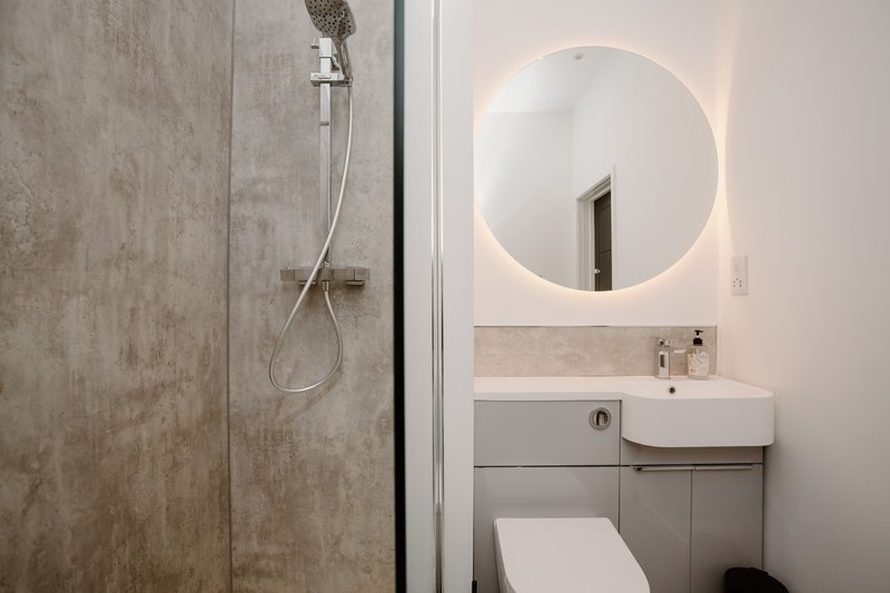 Modern bathroom with walk-in shower, circular illuminated mirror, and white sink vanity