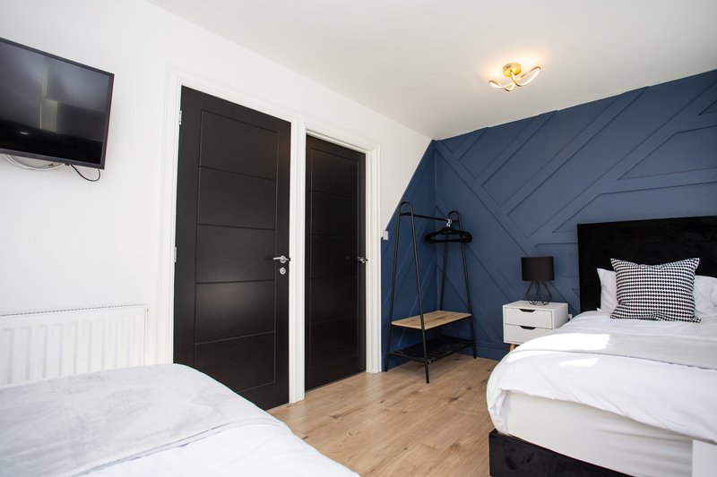 Modern bedroom with two beds, dark blue accent wall, black doors and wooden flooring