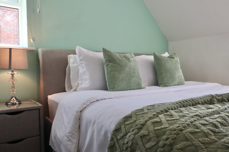Bedroom with double bed, green accent pillows, white bedding, and bedside lamp