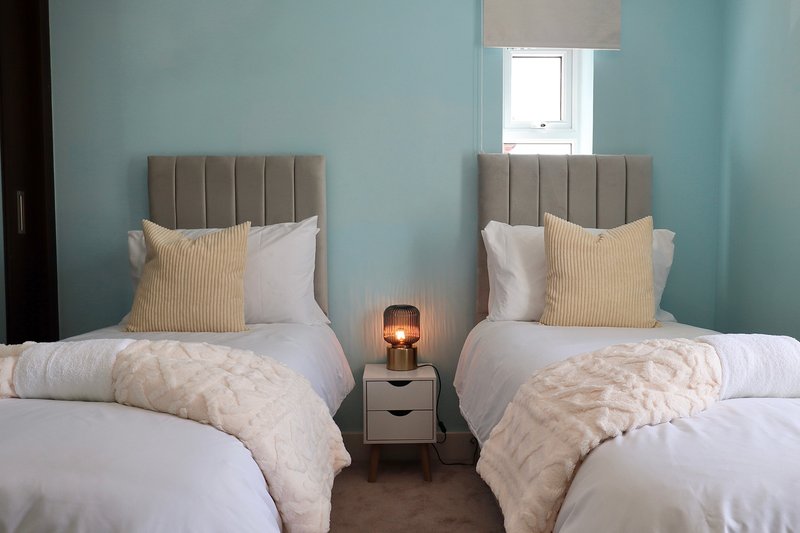 Twin bedroom with two single beds, grey headboards, pale blue walls and small bedside lamp