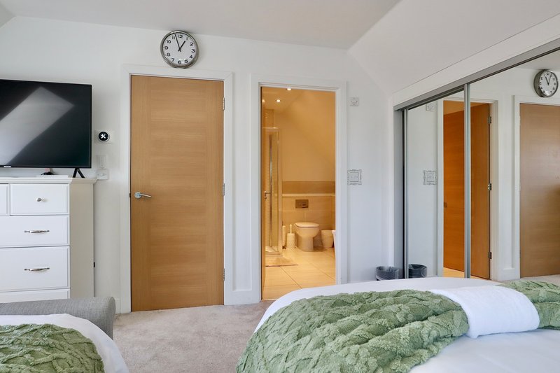 Modern bedroom with twin beds, wooden doors, ensuite bathroom, and wall-mounted clock