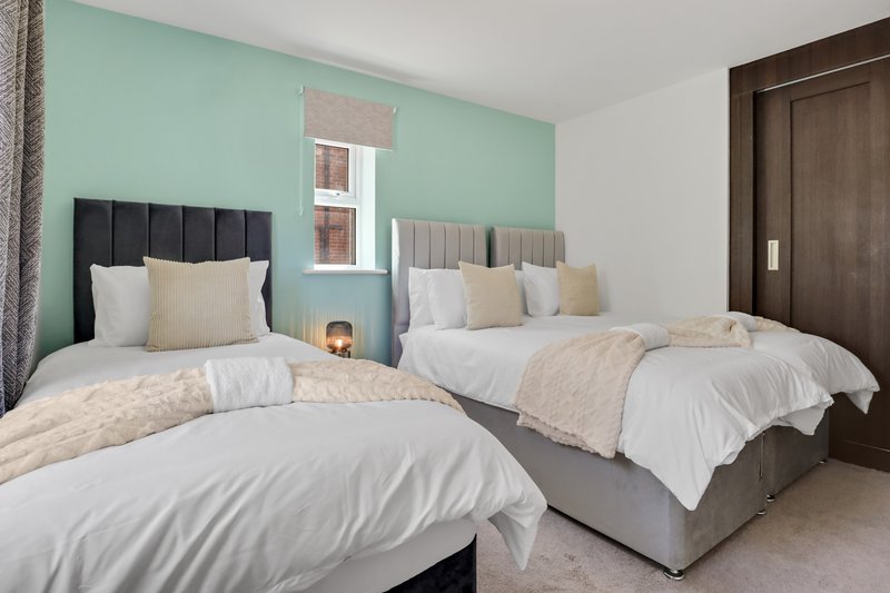 Twin bedroom with two beds, turquoise accent wall, dark wood door and window