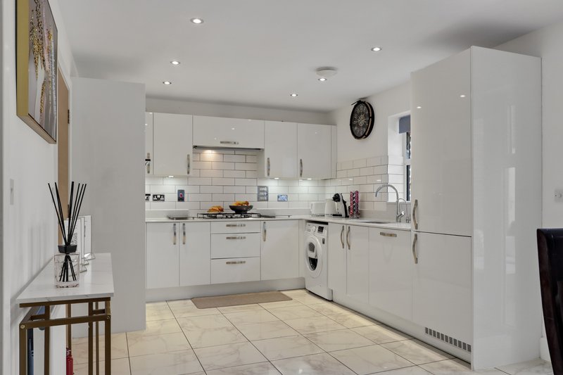 Modern white kitchen with built-in appliances, tile backsplash, and cream flooring