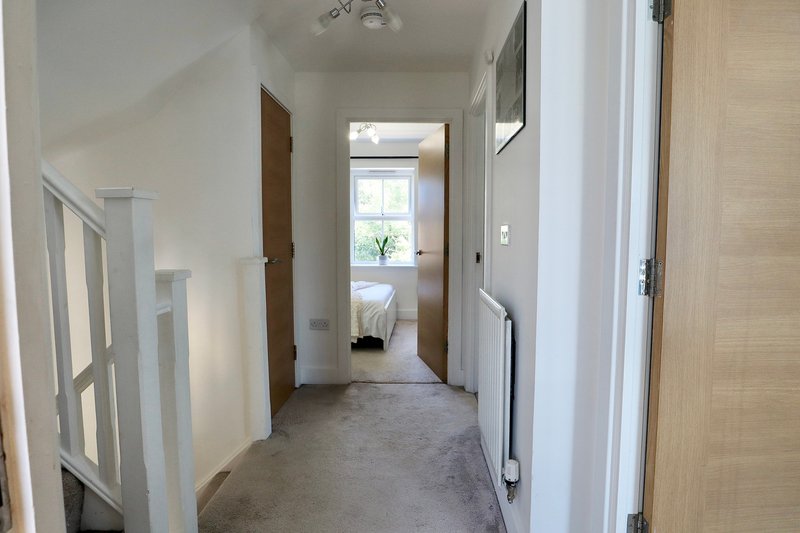 Bright hallway with white walls, wooden doors, and carpet flooring leading to rooms