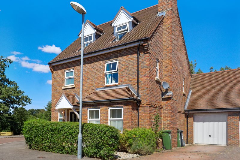 Brick residential house with driveway, garage, and mature hedging in clear daylight