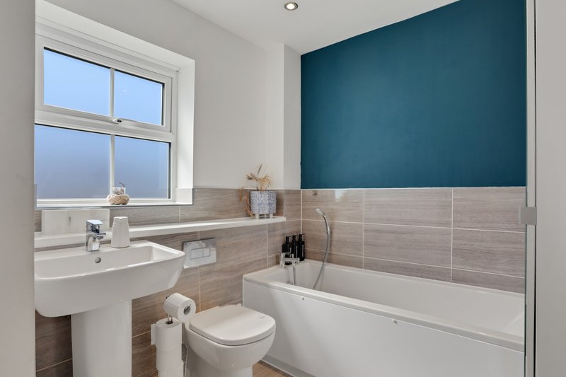 Modern bathroom with white sink, toilet, bathtub, teal accent wall and window