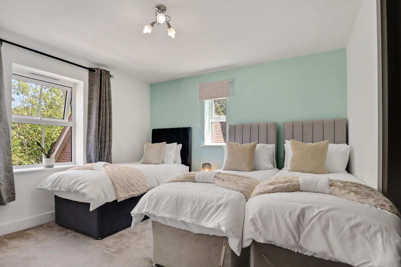 Bright bedroom with two double beds, mint green accent wall, large window and neutral bedding