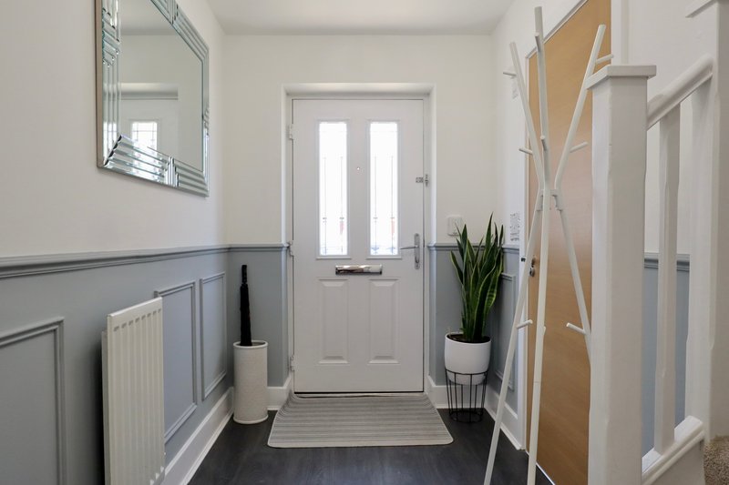 Bright hallway with white door, radiator, mirror, potted plant and striped runner rug