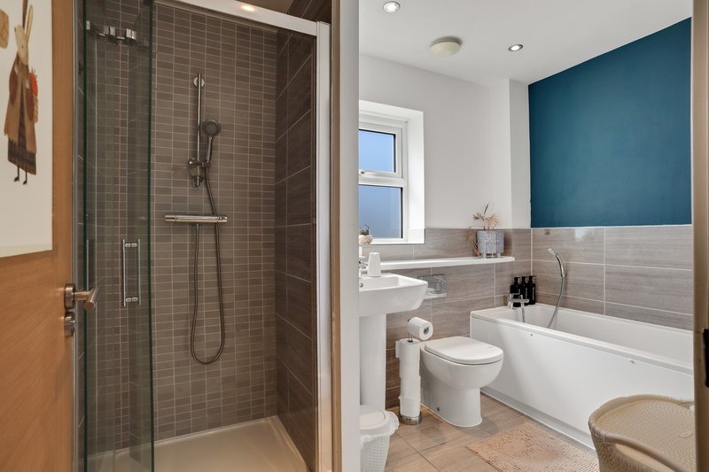 Modern bathroom with walk-in shower, white bathtub, toilet, and teal accent wall