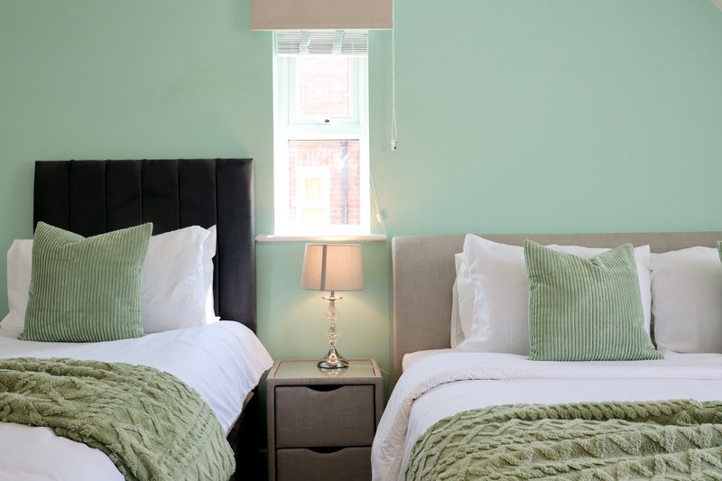 Twin bedroom with green and white bedding, black headboard, lamp and window