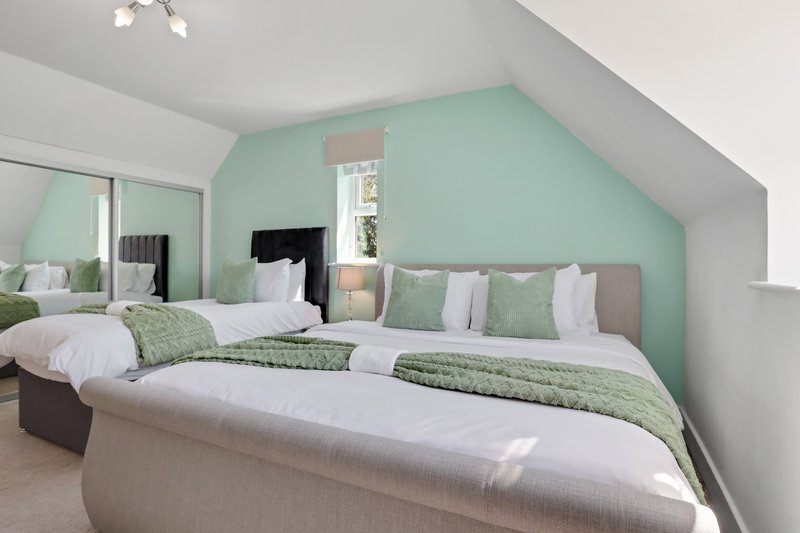Bright attic bedroom with twin beds, mint green accent wall, white ceiling and mirror