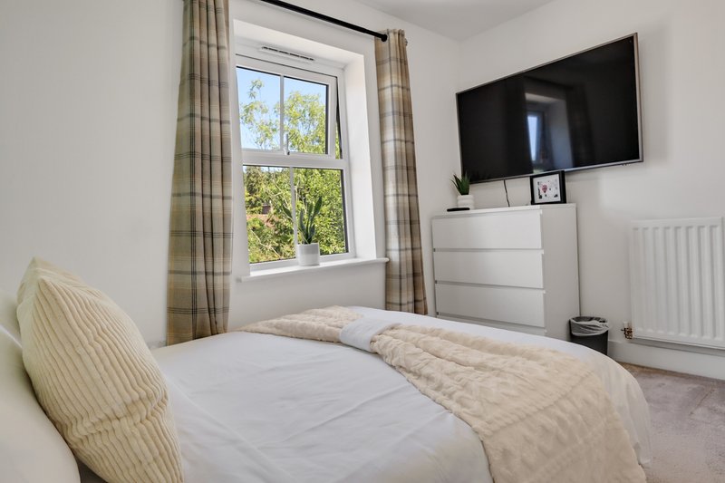 Bright bedroom with double bed, window view, wall-mounted TV, and cream furnishings