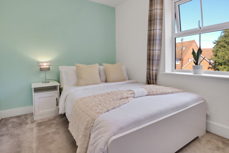 Bright bedroom with double bed, mint green accent wall, bedside lamp and window view