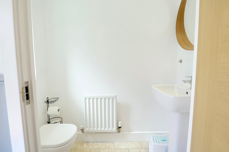 Bright modern bathroom with white sink, radiator, toilet and wooden-framed mirror
