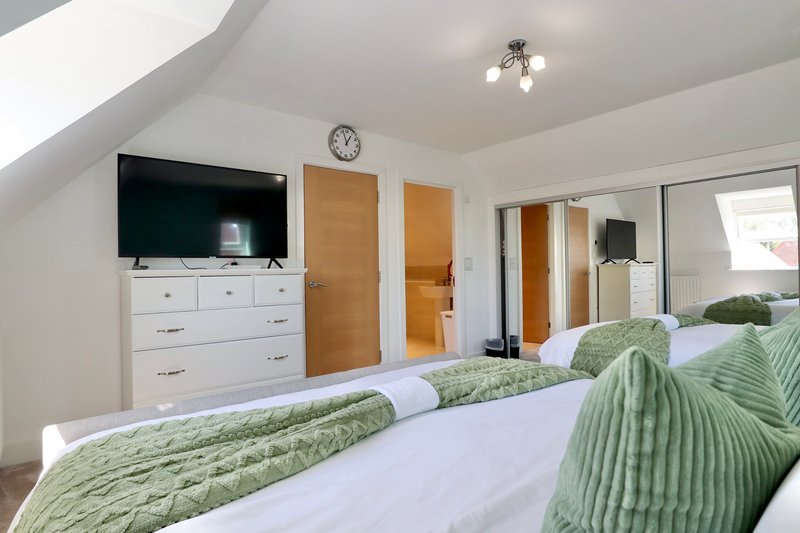 Bright attic bedroom with twin beds, green bedding, white dresser and wall-mounted TV