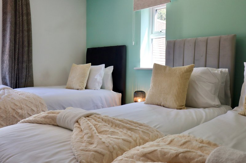 Bright bedroom with two single beds, green accent wall, and window with natural light