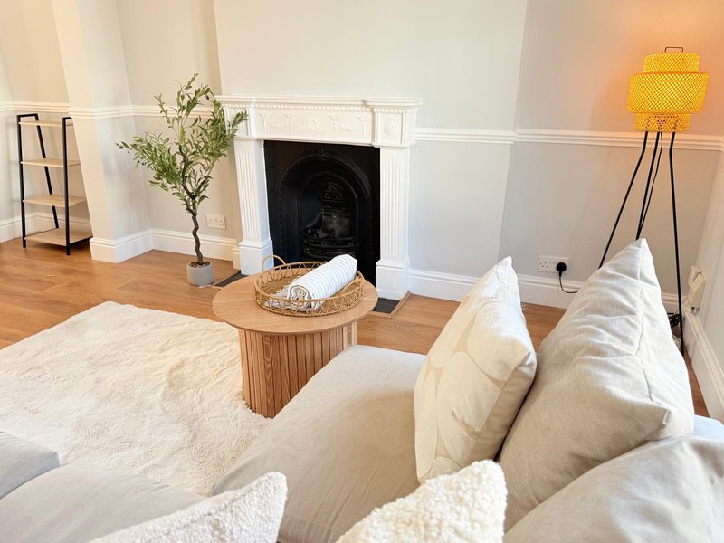 Bright living room with cream sofa, fireplace, wooden coffee table, potted plant and floor lamp