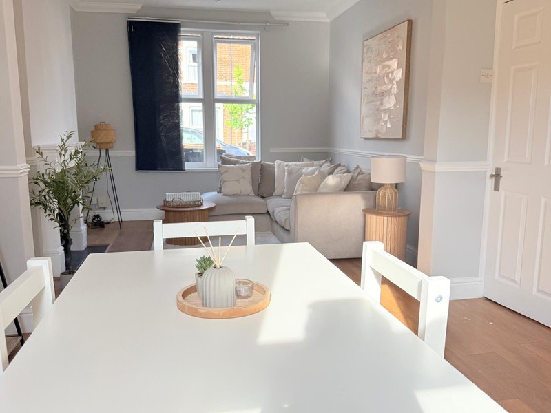 Open-plan living and dining area with white table, grey sofa, and large windows with dark curtains