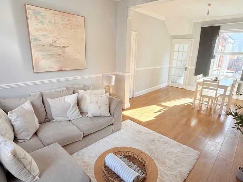 Bright living room with gray sofa, wooden flooring, and open-plan dining area visible beyond