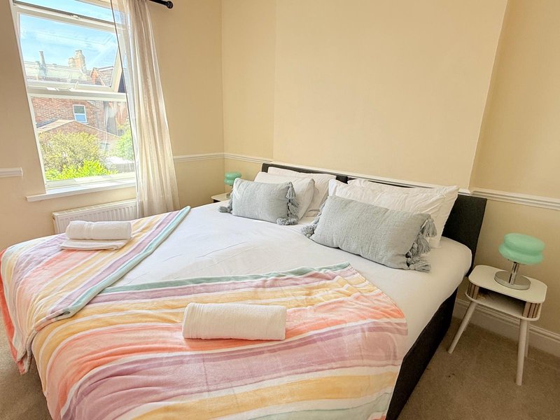 Bright bedroom with double bed, colorful bedding, white nightstand and window with street view