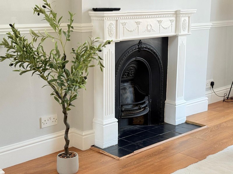 Living room with wooden floor, potted plant, ornate white fireplace with black insert