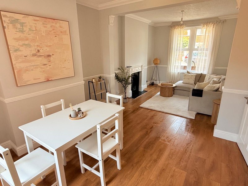 Open-plan living and dining area with white table, fireplace, sofa and large windows