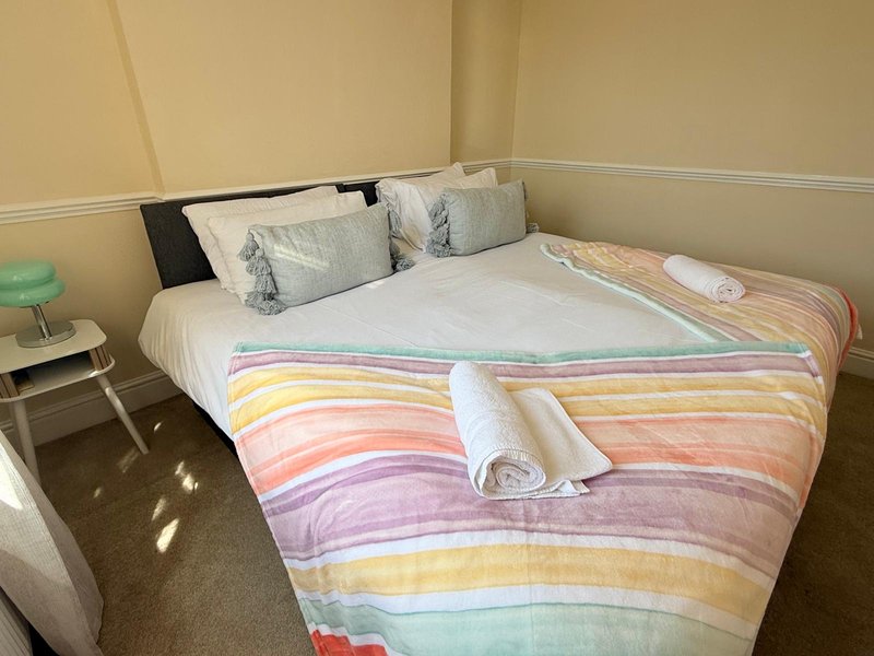 Bedroom with double bed, colorful striped bedding, pillows, and small side table