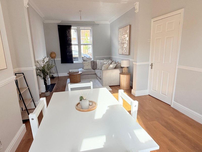 Bright open-plan living space with white dining table, wooden floors, and seating area by window