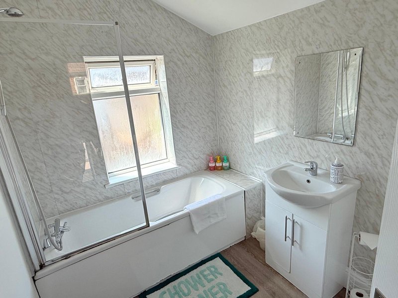 Modern bathroom with bathtub, shower screen, pedestal sink and mirror
