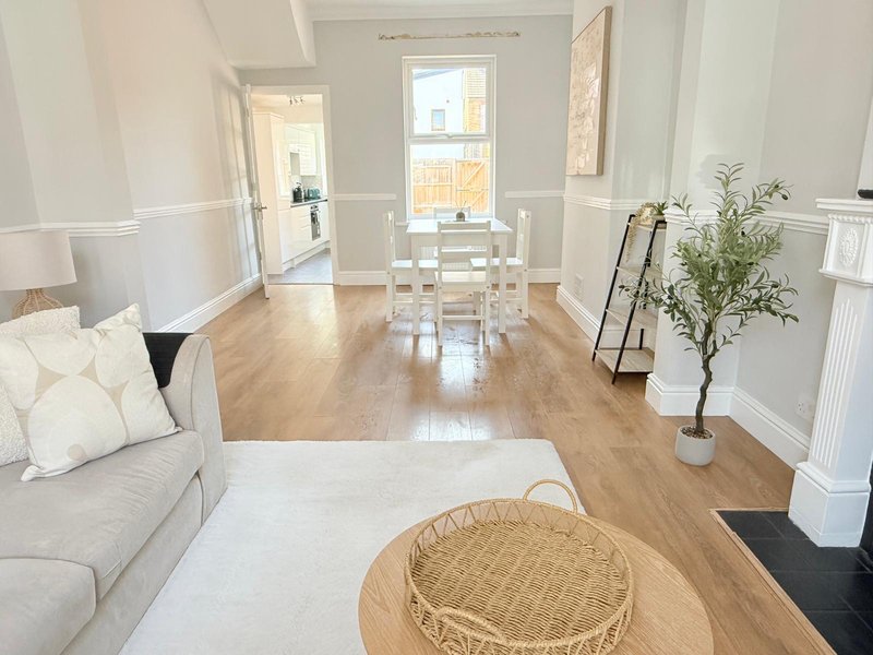 Bright open-plan living room with sofa, wooden dining table, potted plant and hardwood flooring